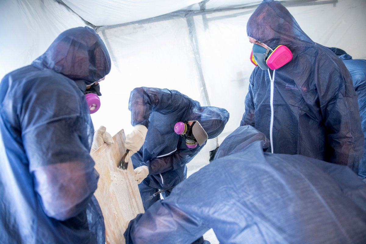 trainees in hazmat suits scraping off paint